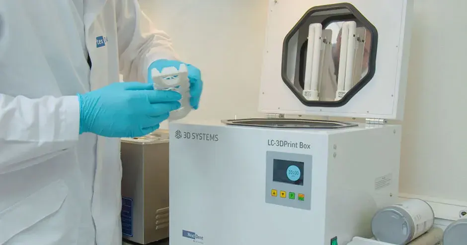 Person mit einem Zahnersatz aus einer Nachbearbeitungsmaschine in der Hand