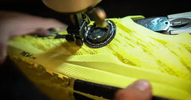Nahaufnahme eines gelben Schuhs, in den ein schwarzes, rundes, 3D-gedrucktes Teil eingenäht wird