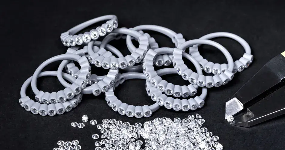 Viele in Wachs geformte Ringe mit eingefassten Diamanten, Spitze eines Messschiebers hält einen Diamanten, verstreute Diamanten