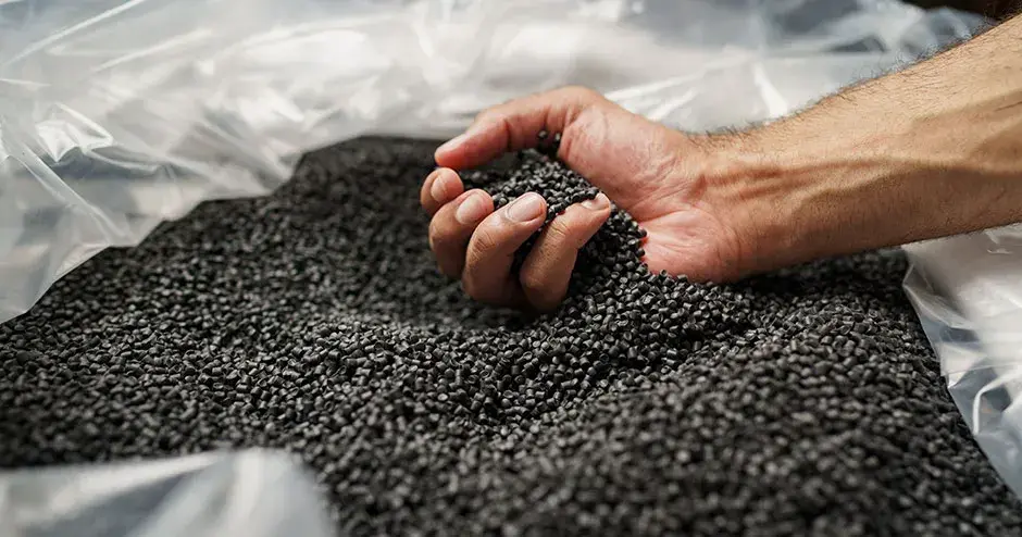 Die Hand einer Person, die schwarze Plastikpellets aufnimmt